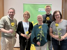 Der neue Vorstand des Kreisverbands Bündnis 90/Die Grünen in Roth steht lächelnd zusammen und hält jeweils eine Sonnenblume in den Händen. Zu sehen sind: Martin Mändl, Tanja Josche, Henrik Schmidt-Heck, Ursula Burkhardt und Eva Neubert. Im Hintergrund ist ein grünes Banner der Partei zu sehen.