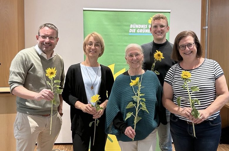 Der neue Vorstand des Kreisverbands Bündnis 90/Die Grünen in Roth steht lächelnd zusammen und hält jeweils eine Sonnenblume in den Händen. Zu sehen sind: Martin Mändl, Tanja Josche, Henrik Schmidt-Heck, Ursula Burkhardt und Eva Neubert. Im Hintergrund ist ein grünes Banner der Partei zu sehen.